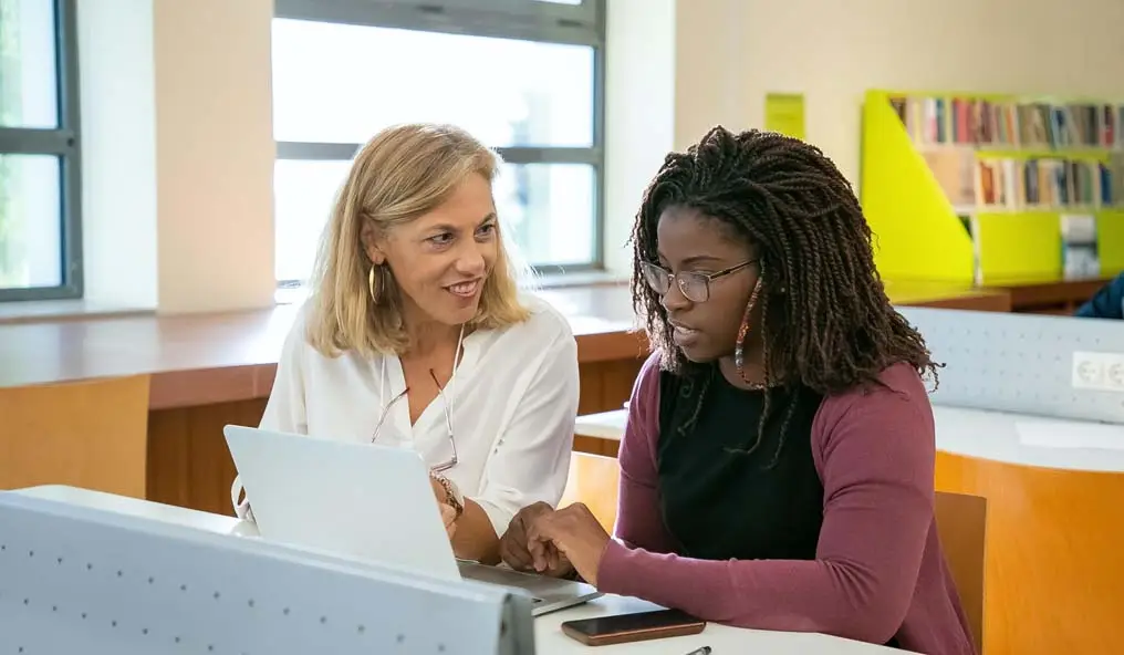 A female student and lecturer sat in front of a laptop chatting