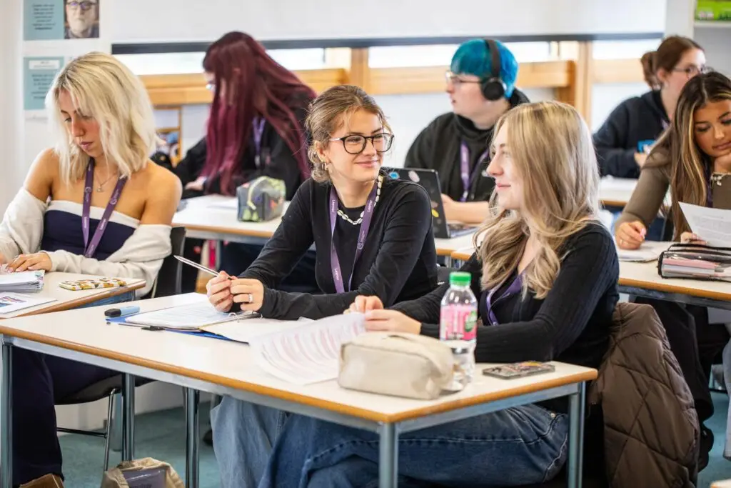 students in a full classroom, with two female students talking and smiing