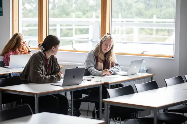 two female students sat together at a desk with laptops